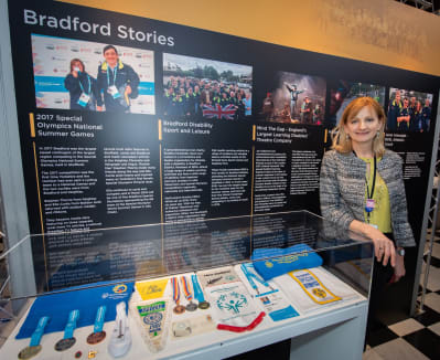 Vicky Hope-Walker standing next to the Bradford stories exhibition display at Cartwright Hall Art Gallery